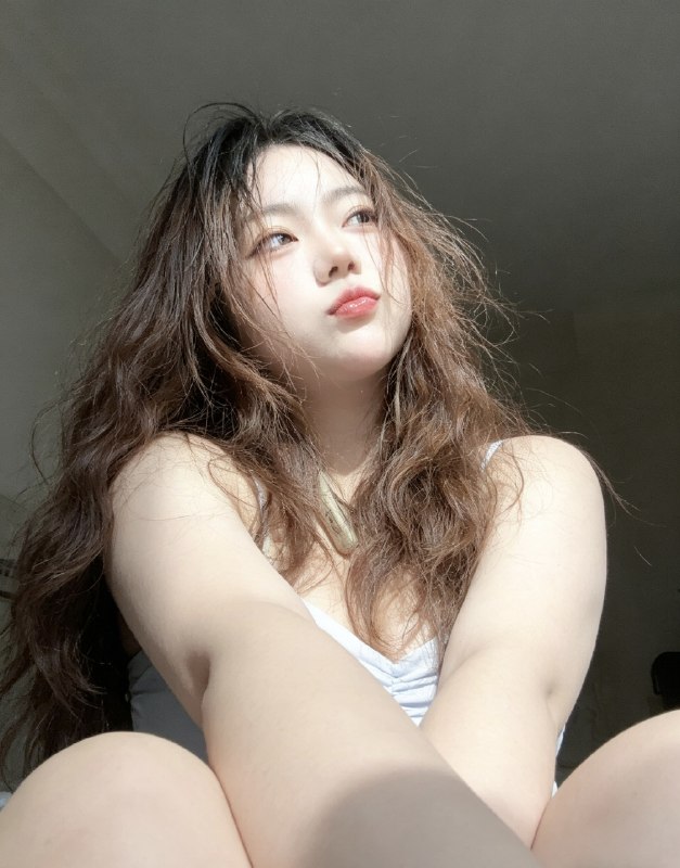 分享一个魔法提示词，坐等美女们返图以照片中的人物为原型，生成9张不同姿势的写真 不要项链，不要背包，低角度仰拍，画面微倾斜，营造随性抓拍感，直接复制就能用，轻松拍出纯欲氛围感写真，背景为色调偏中性且模糊的昏暗房间，年轻的韩系美女，冷白色的皮肤，一头深棕色的长波浪卷发显得有些凌乱，发丝随意地垂落在脸庞和眼睛上，身着一件细肩带的浅色上衣，脸上带着一种微妙的纯欲表情，半睁着慵懒的双眼微微向右看，双唇丰满且带着光泽，呈现出粉中透红的颜色，嘴唇微微撅起，流露出柔和的忧郁又诱人的气质，双手托着头，手指轻按脸颊、双手托腮，手指轻按脸颊，手肘自然支撑，无浓妆，仅唇部有光泽感，突出原生妆容质感