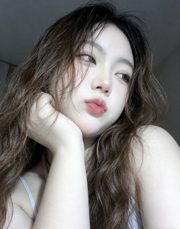 分享一个魔法提示词，坐等美女们返图以照片中的人物为原型，生成9张不同姿势的写真 不要项链，不要背包，低角度仰拍，画面微倾斜，营造随性抓拍感，直接复制就能用，轻松拍出纯欲氛围感写真，背景为色调偏中性且模糊的昏暗房间，年轻的韩系美女，冷白色的皮肤，一头深棕色的长波浪卷发显得有些凌乱，发丝随意地垂落在脸庞和眼睛上，身着一件细肩带的浅色上衣，脸上带着一种微妙的纯欲表情，半睁着慵懒的双眼微微向右看，双唇丰满且带着光泽，呈现出粉中透红的颜色，嘴唇微微撅起，流露出柔和的忧郁又诱人的气质，双手托着头，手指轻按脸颊、双手托腮，手指轻按脸颊，手肘自然支撑，无浓妆，仅唇部有光泽感，突出原生妆容质感