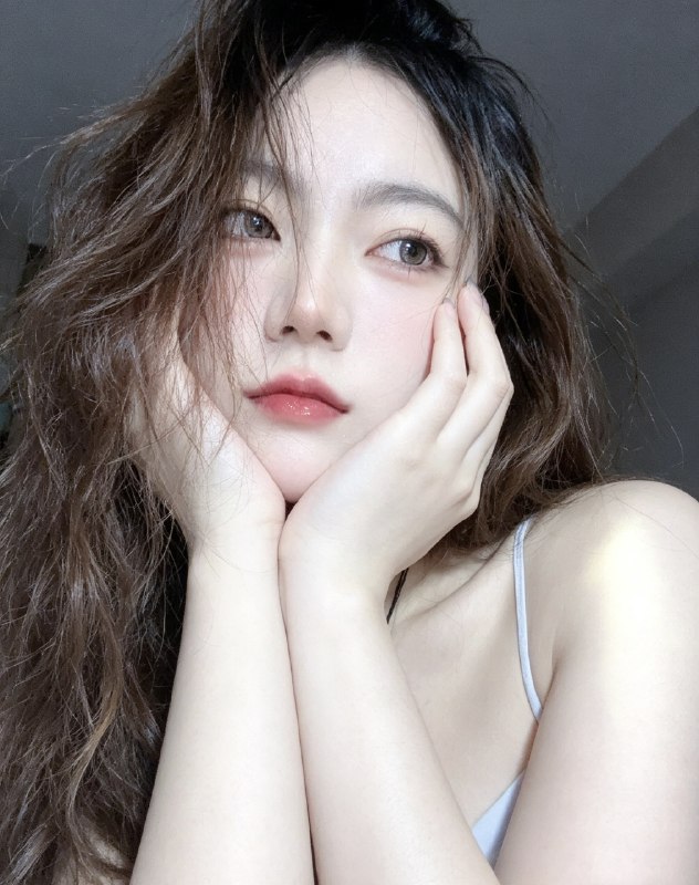 分享一个魔法提示词，坐等美女们返图以照片中的人物为原型，生成9张不同姿势的写真 不要项链，不要背包，低角度仰拍，画面微倾斜，营造随性抓拍感，直接复制就能用，轻松拍出纯欲氛围感写真，背景为色调偏中性且模糊的昏暗房间，年轻的韩系美女，冷白色的皮肤，一头深棕色的长波浪卷发显得有些凌乱，发丝随意地垂落在脸庞和眼睛上，身着一件细肩带的浅色上衣，脸上带着一种微妙的纯欲表情，半睁着慵懒的双眼微微向右看，双唇丰满且带着光泽，呈现出粉中透红的颜色，嘴唇微微撅起，流露出柔和的忧郁又诱人的气质，双手托着头，手指轻按脸颊、双手托腮，手指轻按脸颊，手肘自然支撑，无浓妆，仅唇部有光泽感，突出原生妆容质感