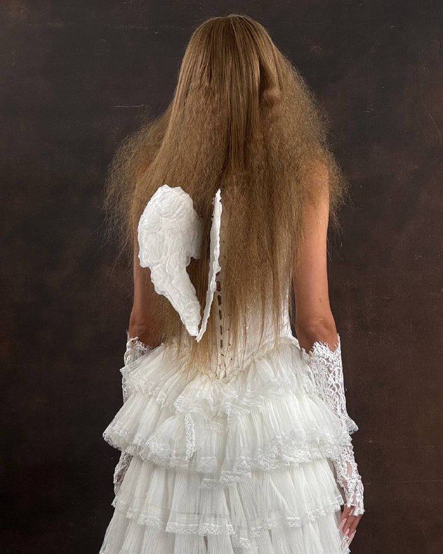 Подготовка парика к укладке и работа с текстуройБаза: нанесла термозащиту и выпрямила волосы стайлером на 180°C. Тем самым создала гладкое полотно, от которого можно строить текстуру.Текстура и выбор инструмента: изначально рассматривала афро-плойку, но она давала бы более круглый, «понятный» завиток. Для нужного характера образа RARA требовалась более модная, ломаная текстура, от рисунка переходящая во взрывной объём. Поэтому выбрала технику накрутки на шпильки.Формирование рисунка: выделяя небольшие пряди, накручивала их на шпильки с низкой оттяжкой — так после вычёсывания сохраняется характерная линия в начале завитка, а длина легко раскрывается в объём.Фиксация: прогревала пряди стайлером, затем дала им полностью остыть.Финиш: сняла шпильки и аккуратно вычесала волосы до нужной формы и распределения текстур. Моя цель — сохранить рисунок, воздух между прямыми и накрученными секциями, и форму, которая выглядит современно.Так парик перестал быть просто заменой волос — он стал частью образа, усилил стилистику бренда и позволил показать модель в новом художественном диапазоне.P.S. На сторис модели ответили сотни подписчиков — многие писали, что с этими волосами она помолодела минимум на 15 лет 😄🫢Подготовка парика к укладке и работа с текстуройБаза: нанесла термозащиту и выпрямила волосы стайлером на 180°C. Тем самым создала гладкое полотно, от которого можно строить текстуру.Текстура и выбор инструмента: изначально рассматривала афро-плойку, но она давала бы более круглый, «понятный» завиток. Для нужного характера образа RARA требовалась более модная, ломаная текстура, от рисунка переходящая во взрывной объём. Поэтому выбрала технику накрутки на шпильки.Формирование рисунка: выделяя небольшие пряди, накручивала их на шпильки с низкой оттяжкой — так после вычёсывания сохраняется характерная линия в начале завитка, а длина легко раскрывается в объём.Фиксация: прогревала пряди стайлером, затем дала им полностью остыть.Финиш: сняла шпильки и аккуратно вычесала волосы до нужной формы и распределения текстур. Моя цель — сохранить рисунок, воздух между прямыми и накрученными секциями, и форму, которая выглядит современно.Так парик перестал быть просто заменой волос — он стал частью образа, усилил стилистику бренда и позволил показать модель в новом художественном диапазоне.P.S. На сторис модели ответили сотни подписчиков — многие писали, что с этими волосами она помолодела минимум на 15 лет 😄🫢