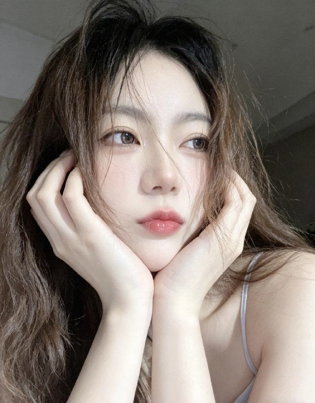 分享一个魔法提示词，坐等美女们返图以照片中的人物为原型，生成9张不同姿势的写真 不要项链，不要背包，低角度仰拍，画面微倾斜，营造随性抓拍感，直接复制就能用，轻松拍出纯欲氛围感写真，背景为色调偏中性且模糊的昏暗房间，年轻的韩系美女，冷白色的皮肤，一头深棕色的长波浪卷发显得有些凌乱，发丝随意地垂落在脸庞和眼睛上，身着一件细肩带的浅色上衣，脸上带着一种微妙的纯欲表情，半睁着慵懒的双眼微微向右看，双唇丰满且带着光泽，呈现出粉中透红的颜色，嘴唇微微撅起，流露出柔和的忧郁又诱人的气质，双手托着头，手指轻按脸颊、双手托腮，手指轻按脸颊，手肘自然支撑，无浓妆，仅唇部有光泽感，突出原生妆容质感