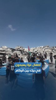בין הריסות בתים הרוסים בעזה, ילדים משחקים בבריכות מים ארעיות, בעוד הדגל הפלסטיני מתנוסס מעל ההריסות, במראה…