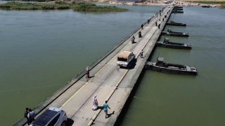 מראות של כלי רכב ואנשים שחוצים את הגשר הצבאי הצף בדיר א-זור.