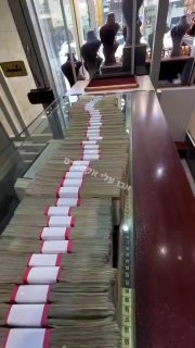 צפו: כך נראים 300 דולר בריאל איראני, שורה באורך מטרים של שטרות כסף ארוזים על פני דלפק בחנות.