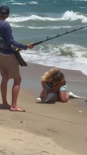 Sandy Beach, Florida: Pliers in hand, a woman kneels next to a shark on the beach and pulls a fishing lure from its jaws before sending it back into the water.