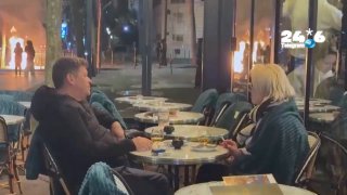 🇮🇱 Spouses are sitting comfortably, drinking and smoking while there are demonstrations in Paris. In Paris, a couple sits peacefully drinking a drink, smoking in a business near the Arc de Triomphe, while nearby, protests continue and a trash can burns.