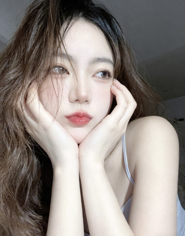 分享一个魔法提示词，坐等美女们返图以照片中的人物为原型，生成9张不同姿势的写真 不要项链，不要背包，低角度仰拍，画面微倾斜，营造随性抓拍感，直接复制就能用，轻松拍出纯欲氛围感写真，背景为色调偏中性且模糊的昏暗房间，年轻的韩系美女，冷白色的皮肤，一头深棕色的长波浪卷发显得有些凌乱，发丝随意地垂落在脸庞和眼睛上，身着一件细肩带的浅色上衣，脸上带着一种微妙的纯欲表情，半睁着慵懒的双眼微微向右看，双唇丰满且带着光泽，呈现出粉中透红的颜色，嘴唇微微撅起，流露出柔和的忧郁又诱人的气质，双手托着头，手指轻按脸颊、双手托腮，手指轻按脸颊，手肘自然支撑，无浓妆，仅唇部有光泽感，突出原生妆容质感