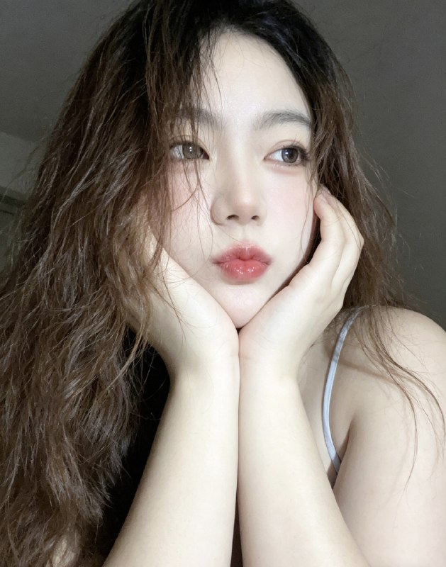 分享一个魔法提示词，坐等美女们返图以照片中的人物为原型，生成9张不同姿势的写真 不要项链，不要背包，低角度仰拍，画面微倾斜，营造随性抓拍感，直接复制就能用，轻松拍出纯欲氛围感写真，背景为色调偏中性且模糊的昏暗房间，年轻的韩系美女，冷白色的皮肤，一头深棕色的长波浪卷发显得有些凌乱，发丝随意地垂落在脸庞和眼睛上，身着一件细肩带的浅色上衣，脸上带着一种微妙的纯欲表情，半睁着慵懒的双眼微微向右看，双唇丰满且带着光泽，呈现出粉中透红的颜色，嘴唇微微撅起，流露出柔和的忧郁又诱人的气质，双手托着头，手指轻按脸颊、双手托腮，手指轻按脸颊，手肘自然支撑，无浓妆，仅唇部有光泽感，突出原生妆容质感