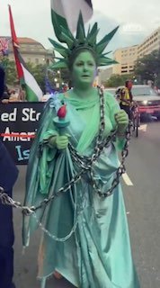 אישה המגלמת את "פסל החירות" באזיקים במזל"ט הסתובבה ברחובות הבירה האמריקאית ביום העצמאות, כדי למחות על "הדומ…