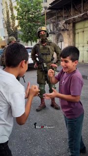 أطفال فلسطينيون يلعبون أمام جنود مسلحين