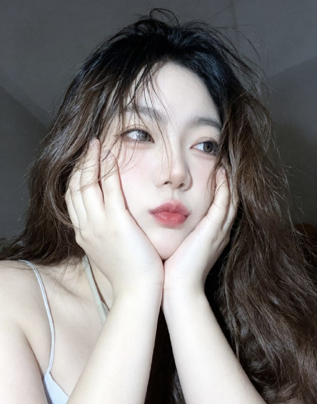 分享一个魔法提示词，坐等美女们返图以照片中的人物为原型，生成9张不同姿势的写真 不要项链，不要背包，低角度仰拍，画面微倾斜，营造随性抓拍感，直接复制就能用，轻松拍出纯欲氛围感写真，背景为色调偏中性且模糊的昏暗房间，年轻的韩系美女，冷白色的皮肤，一头深棕色的长波浪卷发显得有些凌乱，发丝随意地垂落在脸庞和眼睛上，身着一件细肩带的浅色上衣，脸上带着一种微妙的纯欲表情，半睁着慵懒的双眼微微向右看，双唇丰满且带着光泽，呈现出粉中透红的颜色，嘴唇微微撅起，流露出柔和的忧郁又诱人的气质，双手托着头，手指轻按脸颊、双手托腮，手指轻按脸颊，手肘自然支撑，无浓妆，仅唇部有光泽感，突出原生妆容质感