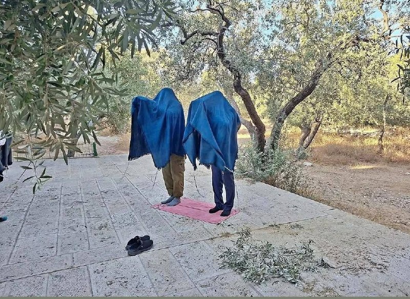 שני מתנחלים עונדים את מטפחת התפילה היהודית "טלית" שראשיהם וגופם מכוסים לחלוטין, והם מניחים על הקרקע מה שמכו…