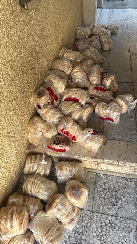 תמונה של תושבים אוספים לחם כדי לחלק לנצורים במחנה קלנדיה, מצפון לירושלים הכבושה.