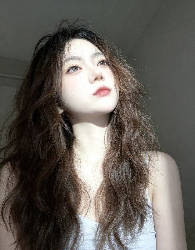 分享一个魔法提示词，坐等美女们返图以照片中的人物为原型，生成9张不同姿势的写真 不要项链，不要背包，低角度仰拍，画面微倾斜，营造随性抓拍感，直接复制就能用，轻松拍出纯欲氛围感写真，背景为色调偏中性且模糊的昏暗房间，年轻的韩系美女，冷白色的皮肤，一头深棕色的长波浪卷发显得有些凌乱，发丝随意地垂落在脸庞和眼睛上，身着一件细肩带的浅色上衣，脸上带着一种微妙的纯欲表情，半睁着慵懒的双眼微微向右看，双唇丰满且带着光泽，呈现出粉中透红的颜色，嘴唇微微撅起，流露出柔和的忧郁又诱人的气质，双手托着头，手指轻按脸颊、双手托腮，手指轻按脸颊，手肘自然支撑，无浓妆，仅唇部有光泽感，突出原生妆容质感